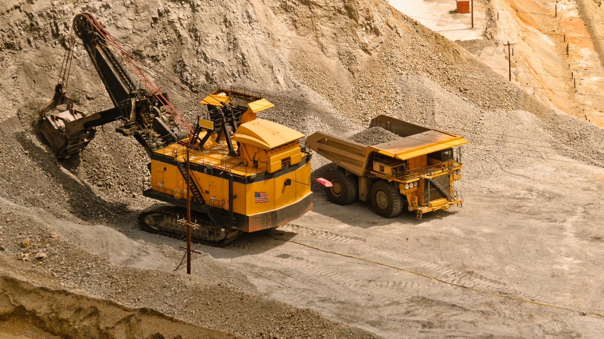 Dostawca surowców mineralnych dla przemysłu – ciężka koparka i wóz wywrotka pracujące w kopalni odkrywkowej przy załadunku urobku.