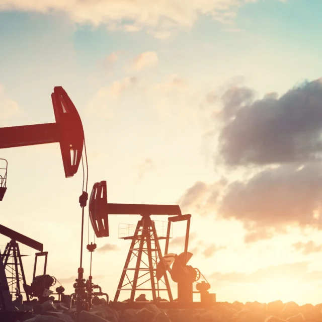 Dystrybutor paliw stałych i surowców energetycznych – pompy wydobywcze ropy naftowej pracujące o zachodzie słońca na tle nieba.