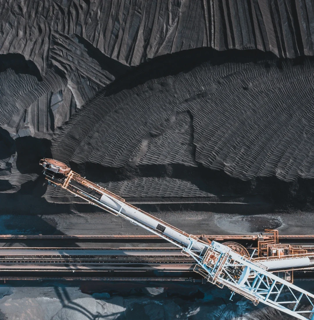 Coal tar supplier – industrial installation with a conveyor belt over coal stockpiles, symbolizing extraction and processing of raw materials.