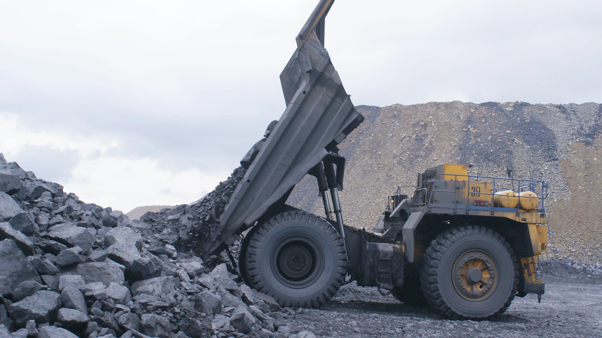 Großhandel mit Kohle — ein leistungsstarker Minen-Dumper mit angehobener Ladefläche, der große Kohlebrocken auf einen Haufen in einem Tagebau entlädt, was das Ausmaß der industriellen Förderung und Verteilung des Rohstoffs zeigt.