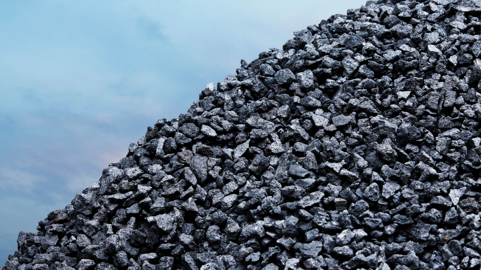 Wholesale coal sales — a tall heap of small, glossy lumps of hard coal rising under an open, bright sky, symbolizing a stock of raw material prepared for mass distribution.